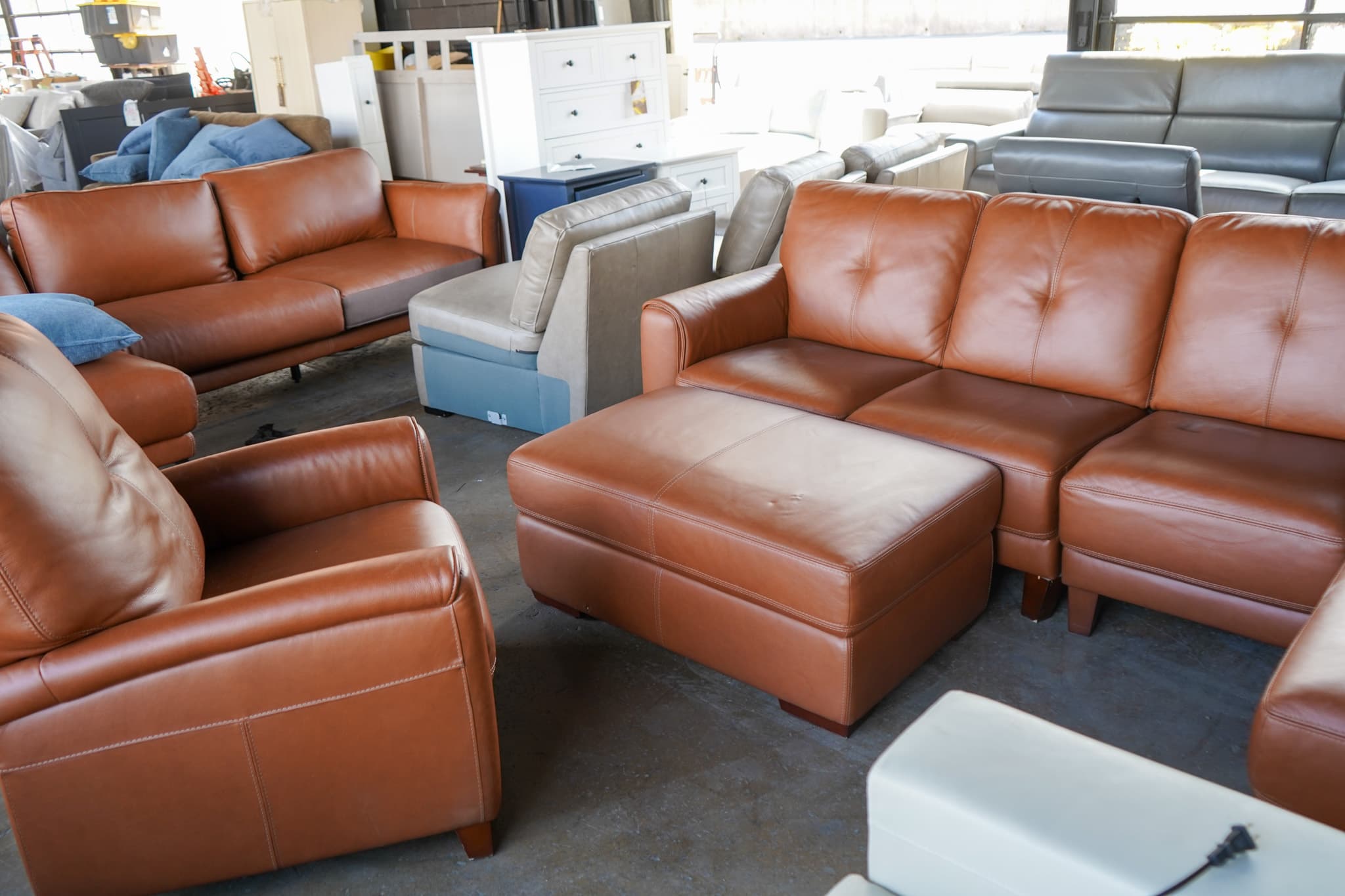 Leather sofa, loveseat, and ottoman staged on the warehouse floor with wrapped pieces behind them